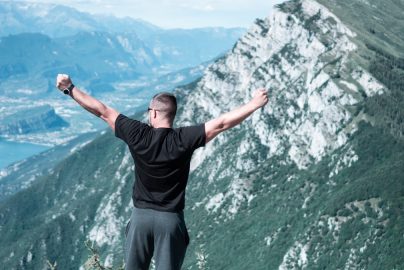 Man standing with arms raised in celebration overlooking a breathtaking mountain landscape.